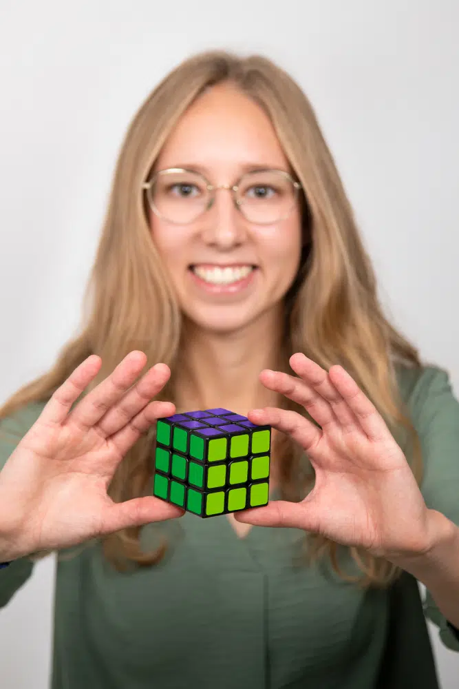 DEBATIN_Produktsparten_Headerbild_DEBADEINS_Simonis_RubikWürfel Sina Simonis is wearing a green blouse and holding up a Rubik's Cube in DEBATIN colors.