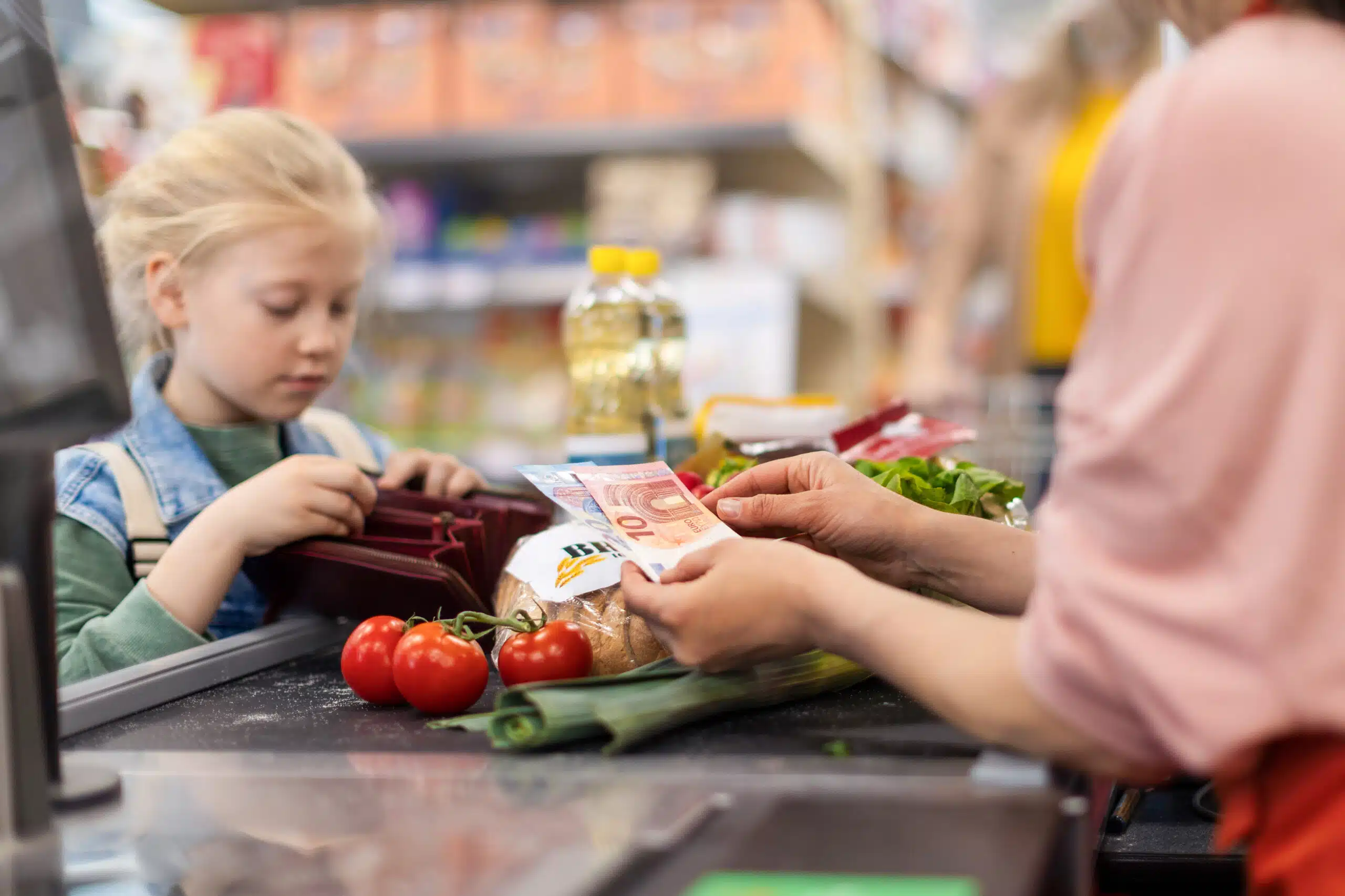 Close-up of little blond girl paying for grocery shopping in supermarket.