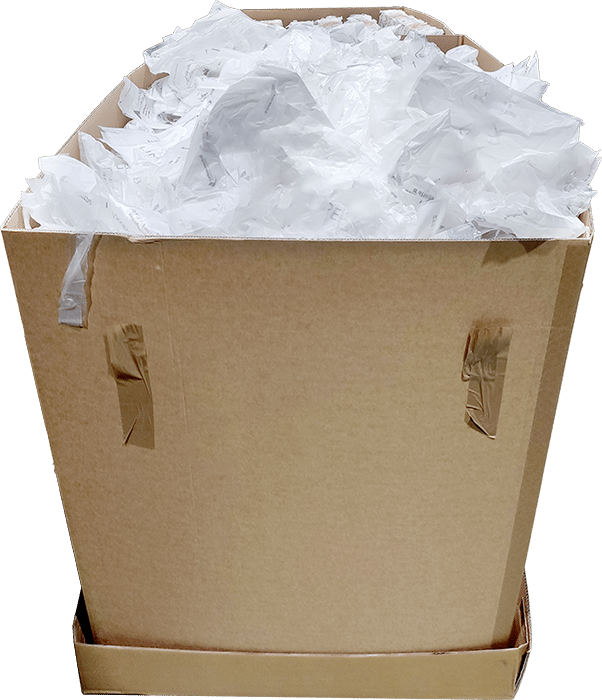 A cardboard box overflowing with loose, crumpled white plastic bags, representing the starting point of collected plastic waste before baling.
