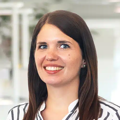 Portrait of Anuschka Gerstl, a smiling woman with long brown hair. She wears a striped blouse in white and black. Anuschka Gerstl works as Sales Consultant / Customer Service at DEBATIN.
