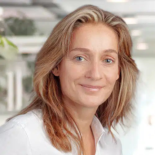 Portrait of Eva-Maria Schneider, a woman with shoulder-length brown-blonde hair, smiling kindly at the camera and wearing a white shirt. She works as Sales Consultant / Customer Service at Debatin.