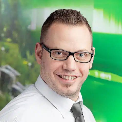 Portrait of Florian Klonig, Head of Shipping Department at Debatin. His broad smile and distinctive glasses shape his face, framed by short dark hair and a neat beard.