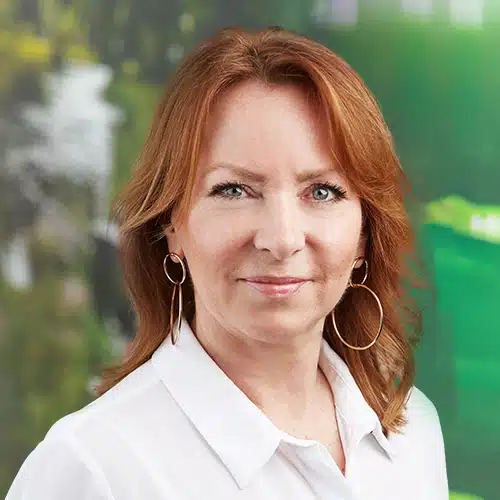 Portrait of Francoise Mathieu, Sales Support at Debatin. She smiles softly at the camera, has reddish-brown hair and striking golden hoop earrings.
