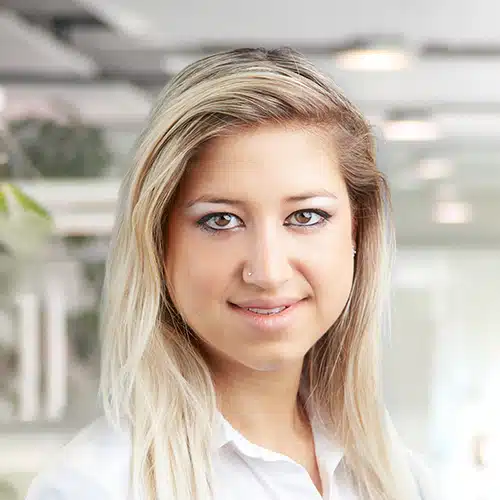 Close-up of Jennifer Petko, Shipping Department at Debatin. Her open smile and long blonde hair stand out. She wears a classic white blouse highlighting her professionalism.