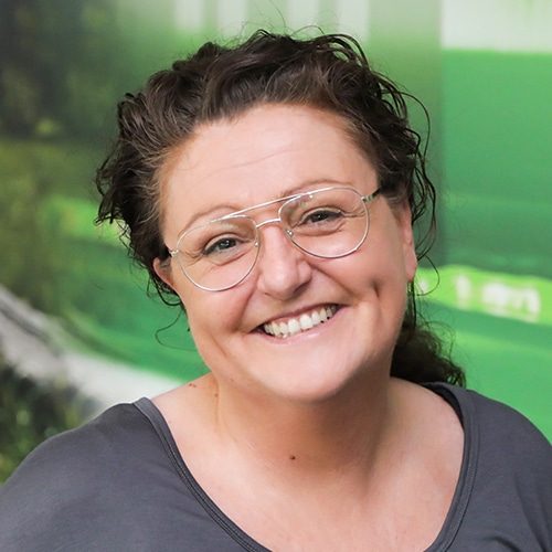 This picture shows Nicole Klingler, Technical Sales Consultant at Debatin. In a close-up, she is smiling, with curly hair, glasses, and a grey top.