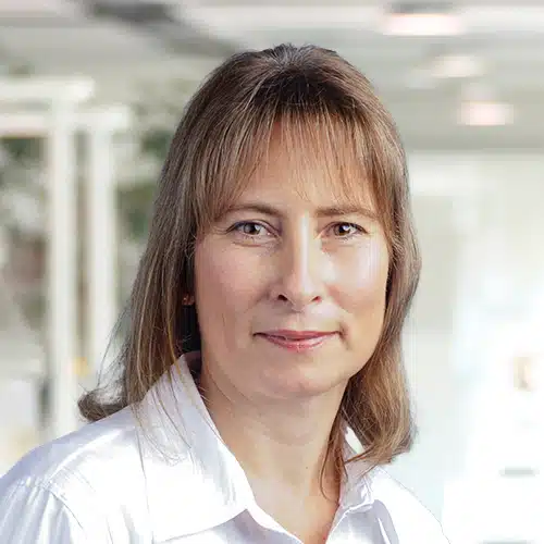 Detail view of Sandra Däschner, Purchasing Department at Debatin. She appears with an open, friendly expression and wears a classic white blouse. Her shoulder-length brown hair frames her face against a softly blurred light background.