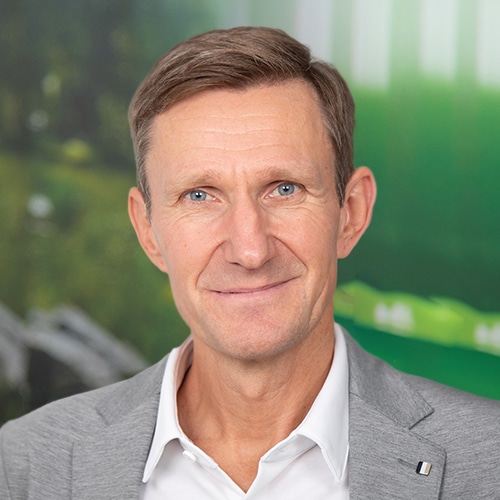Close-up of Thomas Rose, CEO at Debatin. He has a warm, friendly smile and bright eyes. He wears a white shirt under an elegant grey jacket.